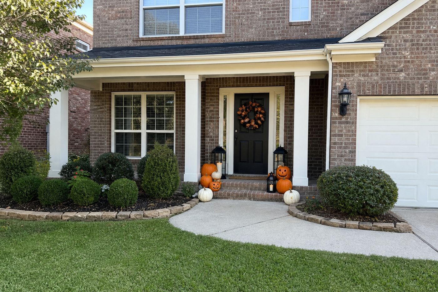 A brick front porch decorated for Halloween with orange and white pumpkins on the steps, carved jack-o'-lanterns, lanterns and a wreath on the door